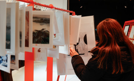 ženska si ogleduje ilustracije, ki so razporejene na stojalu