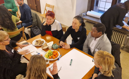 ljudje sedijo za mizo, na njej je velik bel list papirja