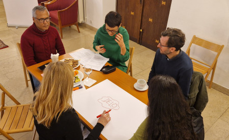 ljudje sedijo za mizo, na njej je velik bel list papirja