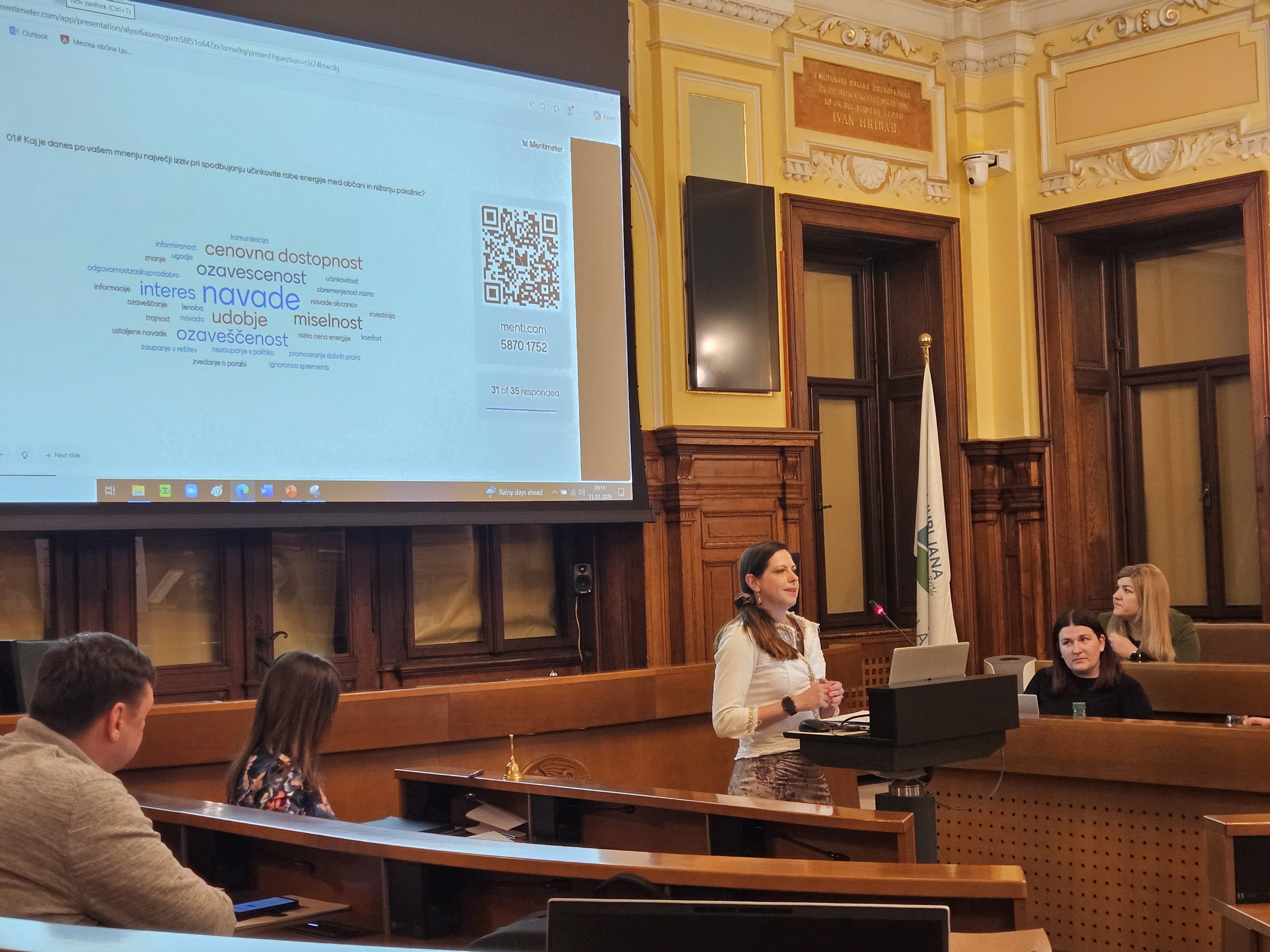 govorec za pultom govori, v ozadju predstavitev