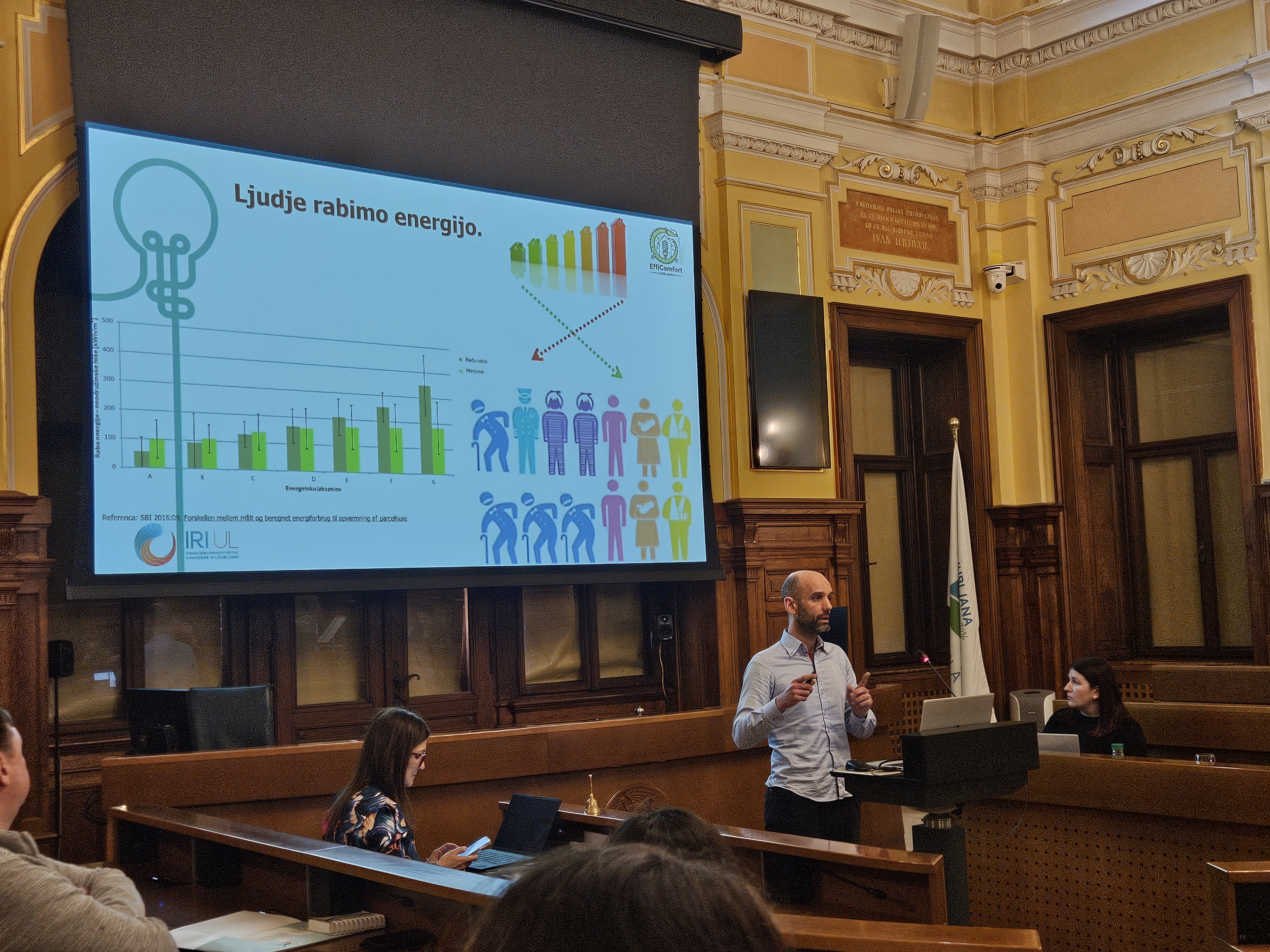 govorec za pultom govori, v ozadju predstavitev