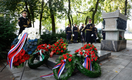 Slovesnost ob polaganju vencev pri Grobnici narodnih herojev, kjer stojijo vojaki v uniformah. Spomenik obdan z venci, vojaki in občinstvom v ozadju.