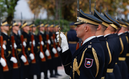 Vojaki garde slovenskih oboroženih sil v uniformah stojijo v vrsti z dvignjenimi puškami med slovesnostjo.