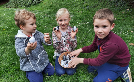 Otroci sedijo na travi in imajo v košarici pirhe, ki so jih našli na lovu za pirhe