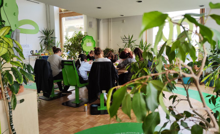 Udeleženci delavnice v Info točki Misija 100 sedijo za mizo, obkroženi so z rastlinami 