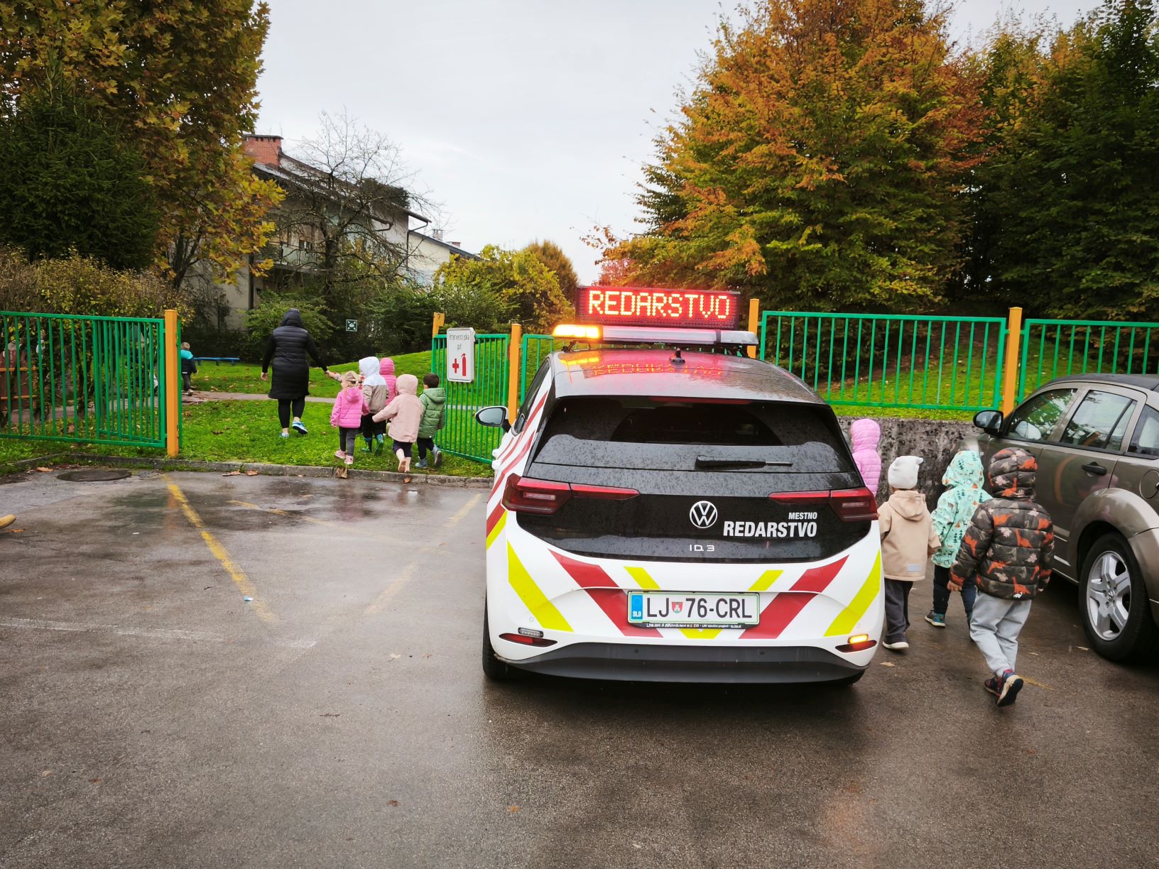 redarski avto pred vrtcem, okoli njega otroci