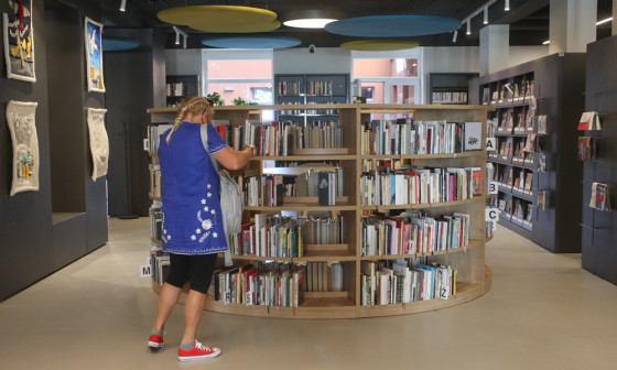 dekle stoji pred knjižno polico