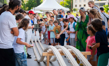 Otroci, starši, dedki in babice po lesenem stojalu spuščajo avtomobilčke