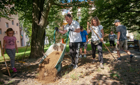 skupina odrasilh in otrok ureja okolico blokov na Ilirski ulici