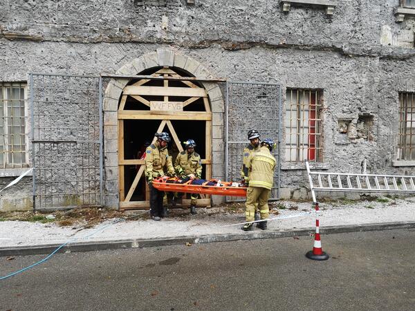 reševalci z ranjencem na nosilih pred poškodovano stavbo