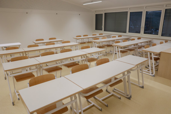 Prenovljena učilnica na Osnovni šoli Danile Kumar z belimi mizami in lesenimi stoli v svetlem prostoru.